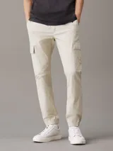Pantalón cargo Calvin Klein Essentials de algodón ripstop elástico color beige claro, con corte skinny, cintura elástica, puños elásticos y bolsillos cargo con solapa.
