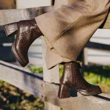 Botas cortas negras de cuero vacuno con textura tipo cocodrilo. Taco de madera forrado en cuero de 8cm, entre suela de goma de 2cm forrada en cuero, inclinación de horma de 6cm y caña de 15cm. Cierre YKK del lado interno y horma de punta cuadrada.