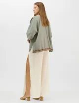 Cardigan tipo kimono de color verde con bordados florales en tono marrón a lo largo de los bordes frontales y en las mangas. Presenta un corte amplio y fluido con mangas tres cuartos.