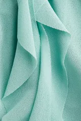 Musculosa de punto color verde menta, con escote en V adornado con volados que caen verticalmente por el centro. El bajo presenta un ruedo con doble capa de volados.