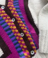 Cardigan tejido a mano en lana merino, con diseño multicolor de bloques geométricos y rayas en tonos blanco, marrón, rosado, celeste y verde. Presenta escote en V, mangas largas y cierre frontal con botones.
