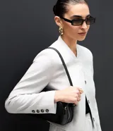 Chaqueta de sastre estructurada color gris claro, con cuello redondo tipo rectilínea, cierre frontal con botones y mangas largas con botones en los puños. Presenta un corte levemente corto y diseño minimalista.