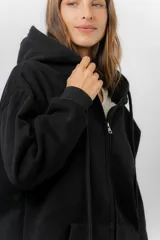 Campera deportiva con capucha de corte oversize, confeccionada en tejido suave con interior forrado en piel sintética. Presenta cierre frontal completo, bolsillos laterales y capucha amplia con cordones largos ajustables.