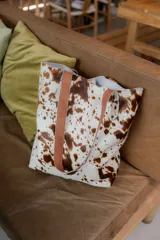 Bolso tipo tote de cuero con pelo color marrón y blanco, con manijas de cuero crudo.