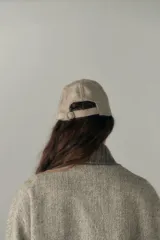 Gorra con visera confeccionada en lana fina sin teñir, con un sutil patrón de tejido en espiga.