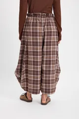 Pantalón de corte holgado con silueta tipo balloon, confeccionado en tela a cuadros. Presenta cintura elástica con cordón ajustable y cortes laterales circulares que aportan volumen a la prenda.