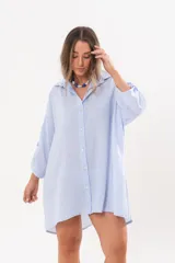 Vestido camisero de lino color celeste, con escote en V, cuello clásico, cierre frontal de botones y mangas tres cuartos regulables. Diseño holgado con corte asimétrico.