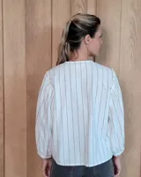 Camisa de manga larga con diseño de rayas verticales y bordados sutiles. Presenta cuello redondo, cierre frontal con botones y mangas abullonadas con volados en los hombros.