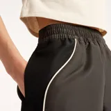 Short New Balance de mujer modelo Trackside, color gris oscuro, con cintura elástica y ribetes contrastantes en los laterales. Presenta el logo de la marca bordado en la pierna izquierda.