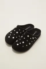 Suecos tipo zueco color negro con acabado de gamuza, decorados con tachas metálicas plateadas circulares. Poseen suela plana y diseño abierto en el talón.
