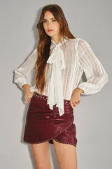 Falda corta cruzada de cuero ovino color bordó, con tachas metálicas plateadas decorando el borde y la cintura.