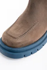 Bota tipo Chelsea de cuero lavado en tono marrón, con paneles laterales elásticos en color marrón oscuro. Presenta una suela track robusta de goma en color azul y un tirador trasero en el mismo tono azul.