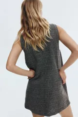 Vestido corto sin mangas, de corte recto, con cuello redondo y cierre frontal de botones. El tejido es tweed o similar, en tonos grises y negros jaspeados.