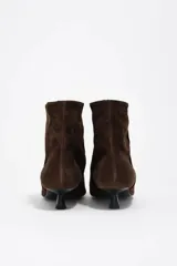 Botín de serraje color marrón con diseño de punta fina y tacón bajo tipo kitten heel de 3,5 cm. Cuenta con forro de piel de cordero y suela de caucho.