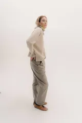 Polera tejida en lambswool color beige, con cuello alto y diseño de intarsia en tonos marrones y grises. Presenta botones forrados en el cuello para modular la apertura.