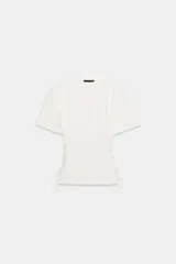 Camiseta blanca de cuello redondo y manga corta, con detalle de cordones ajustables en los laterales.
