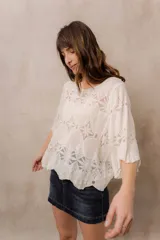Blusa de punto calado color blanco, con diseño geométrico y floral transparente, escote redondo y mangas tres cuartos amplias de calce relajado.