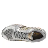 Championes Asics Gel-Kayano 14, de color gris con detalles metalizados plateados y franjas laterales negras con bordes naranjas.