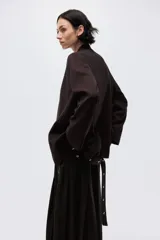 Blazer color marrón oscuro con cuello elevado, hombreras, abertura en los puños y bolsillos delanteros ribeteados. Incluye un cinturón fino con hebilla metálica para ajustar la cintura.