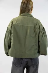 Campera corta de pana color beige, con cuello clásico, cierre frontal con botones y amplios bolsillos con solapa en el pecho. Cuenta con mangas largas abullonadas y diseño holgado.