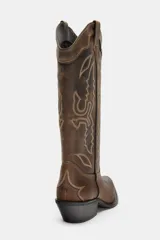 Bota estilo cowboy de piel con efecto desgastado. Presenta bordados decorativos en el cuerpo, doble tirador lateral y tacón medio con acabado en punta.