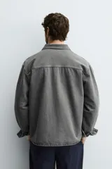 Camisa de denim de algodón, color gris oscuro lavado, de corte holgado (boxy fit). Presenta cuello solapa, manga larga con puño abotonado, bolsillo de plastrón en el pecho y cierre frontal con botones.