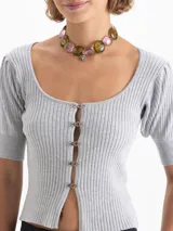 Top de punto acanalado color beige, con escote redondo amplio, mangas cortas abullonadas y cierre frontal mediante ganchos decorativos con piedras.