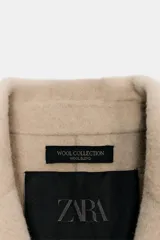Abrigo corto de Zara confeccionado en hilatura con lana, con cuello solapa, manga larga, bolsillos de plastrón en el delantero y cierre frontal con botones.