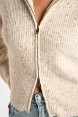 Cardigan de punto acanalado en color beige melange con motas oscuras. Presenta un diseño ajustado al cuerpo, cierre frontal completo con cremallera metálica y cuello alto.