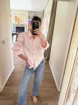 Camisa de algodón color rosado, de corte holgado, con cuello clásico, cierre frontal con botones y mangas largas abullonadas con detalles fruncidos.
