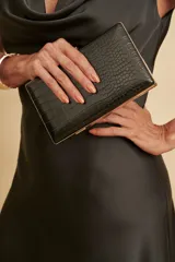 Cartera tipo clutch color negro con diseño texturizado en relieve símil cocodrilo y detalles de herrajes dorados en los bordes.