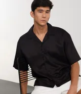 Camisa de lino blanca de corte boxy, manga corta, cuello bowling y cierre frontal de botones.