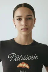 Remera corta de algodón color gris oscuro, con cuello redondo, mangas cortas y estampa frontal con la frase "Pâtisserie Paris" y un dibujo de un croissant.