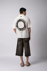 Camisa de manga corta confeccionada en lino, de corte relajado y cuello clásico. Presenta un diseño minimalista en color blanco con textura natural.