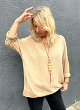 Blusa de corte holgado y diseño minimalista en color camel, con cuello redondo amplio y mangas tres cuartos con dobladillo.