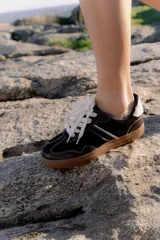 Zapatillas bajas de cuero color marrón oscuro con detalles en blanco y suela de goma color caramelo.