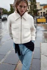 Cazadora de textura suave con cuello solapa, manga larga y cierre frontal con cremallera metálica. Presenta dos bolsillos de plastrón con solapa en la parte delantera.