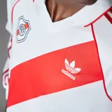 Camiseta de fútbol Adidas de manga larga de River Plate, modelo retro inspirado en 1994. Diseño en color blanco con la tradicional banda roja diagonal, cuello polo, y detalles en rojo en los hombros y las icónicas tres tiras en las mangas.
