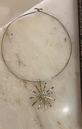 Gargantilla rígida de metal con dije central en forma de sol con rayos alargados y textura martillada.