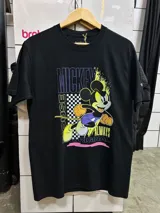 Remera negra de algodón con estampado frontal estilo urbano de Mickey Mouse, con detalles en amarillo, violeta y un patrón ajedrezado.