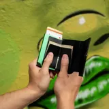 Billetera tipo tarjetero de cuero negro con caja de aluminio interna y sistema de deslizamiento para tarjetas. Cuenta con cierre mediante broche a presión.