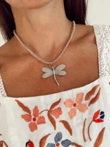 Collar con cordón de seda trenzado en color beige y dije de libélula en acero quirúrgico con acabado texturizado.