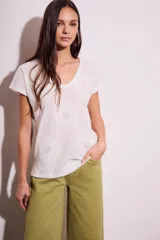Remera de algodón color blanco con cuello en V y mangas cortas. Presenta un diseño con flores bordadas en relieve y detalles calados en el tejido.