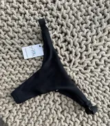 Bottom de bikini colaless negro, sin costuras, con textura de rayitas en la parte delantera y lycra con brillitos en la parte trasera. Breteles regulables en los costados.