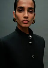Chaqueta recta color negro con cuello mao, cierre frontal y bolsillos delanteros con solapa y botones joya.
