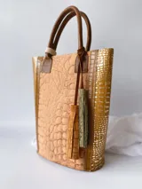 Bolso matero de cuero color beige con textura tipo piel de cocodrilo, detalles en cuero color marrón y borlas decorativas.