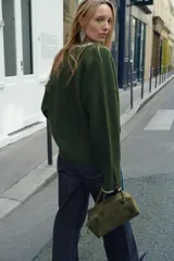 Chaqueta de punto color verde oscuro con cuello redondo y cierre frontal de botones. Presenta detalles de vivos en color crema en el cuello, la tapeta de botones y los puños.