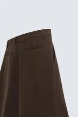 Bermuda de corte regular fit, color marrón oscuro, confeccionada en tejido con lino. Presenta pliegues frontales, bolsillos delanteros y bolsillos traseros de vivo. Cierre frontal con cremallera y botón.