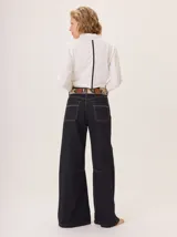 Pantalón ancho de denim oscuro, corte holgado desde la cadera hasta el tobillo, con pespuntes a contratono. Presenta pinzas debajo de la rodilla y bordado de monograma en el bolsillo delantero.