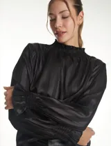 Blusa de satén negro con diseño de rayas verticales tono sobre tono. Presenta cuello alto con detalle de fruncido tipo smock, mangas largas con puños elásticos y terminación con volado.